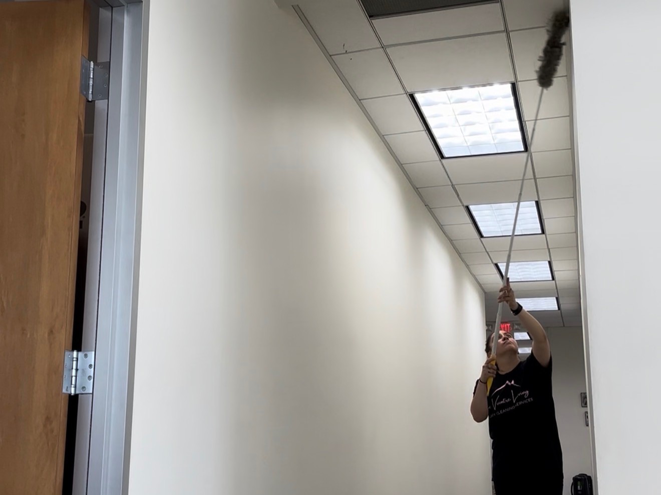 Le Vvintre team member dusting high surfaces in a commercial hallway